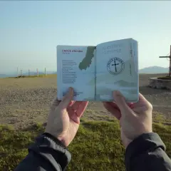 Un passaporto dell'Appennino Modenese, con la Croce Arcana di Fanano, tenuto in mano davanti a un panorama montano e una croce.