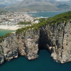La leggenda della Montagna Spaccata a Gaeta: imponenti scogliere rocciose si tuffano nel mare blu, con la città sullo sfondo.