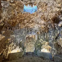 Interno di una grotta con stalattiti e stalagmiti, illuminata da una luce soffusa che filtra da un'apertura in alto. Sembra il ventre del **colosso dell'Appennino**.