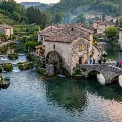 Un incantevole borgo italiano, una vera citta sull'acqua, con case in pietra, un mulino ad acqua e un ponte pittoresco attraversato da persone.