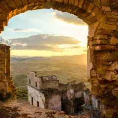 Rovine di **paesi abbandonati in Italia** illuminate dal tramonto, con colline ondulate all'orizzonte.