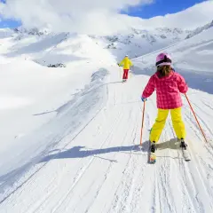 Bambini imparano a sciare su piste da sci per principianti, con montagne innevate sullo sfondo.