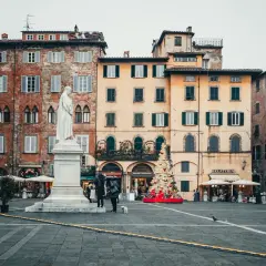 La piazza di Lucca con la statua bianca, edifici storici e un albero di Natale decorato.