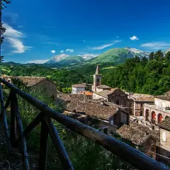 Borgo pittoresco nei Monti Sibillini, cosa vedere: tetti in cotto, campanile e montagne verdi.
