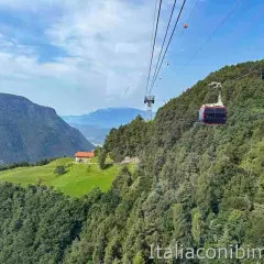 Cabina del trenino del Renon in viaggio tra boschi e montagne, con una casa su un prato verde. Cosa vedere in questo paesaggio mozzafiato.