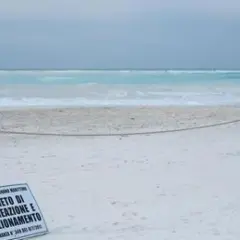 Spiagge bianche deserte con mare turchese. Un cartello vieta balneazione e stazionamento.