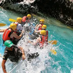 Un gruppo di persone si diverte con il rafting in Emilia Romagna, pagaiando tra spruzzi d'acqua cristallina e rocce.