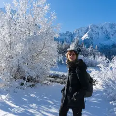 Donna con zaino in un paesaggio invernale innevato, montagne sullo sfondo. Val Saisera incanta con la sua bellezza.