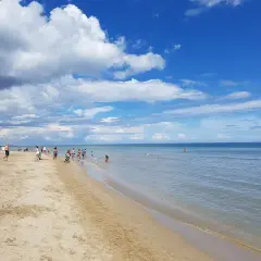 Giornata di sole e nuvole sul mare di Riccione. Bambini giocano sulla battigia mentre adulti passeggiano sulla sabbia dorata.