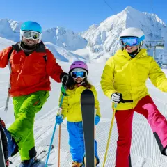 Famiglia felice sulle piste innevate, pronta dove imparare a sciare. Montagne maestose e cielo azzurro fanno da sfondo a questa avventura.
