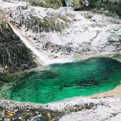 Cascata e pozza smeraldo nella valle del Mis, con rocce bianche e vegetazione.