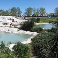 Persone rilassate nelle piscine naturali di acqua termale, un'oasi di pace tra rocce bianche e vegetazione rigogliosa, un vero paradiso per chi cerca le piscine carletti.