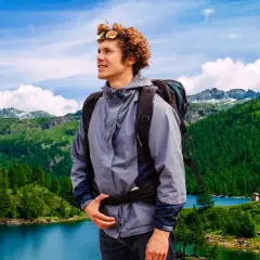 Giovane escursionista con zaino ammira un paesaggio alpino con laghi e boschi nel Piemonte.