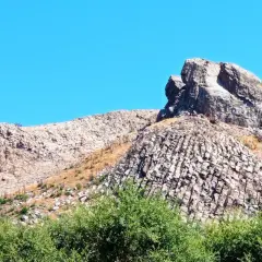 Rocciosa cresta nella Planargia, Sardegna, sotto un cielo azzurro. Vegetazione verde rigogliosa in primo piano.