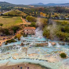 Cascate naturali con acqua azzurra e gente che si rilassa, un vero spettacolo di arte terme in un paesaggio collinare.