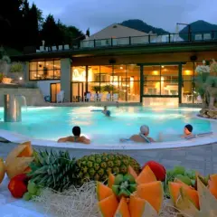 Piscina termale illuminata di notte, con persone che nuotano e un tavolo di frutta fresca in primo piano. Un'oasi di relax che ricorda le terme di Reggio Emilia.
