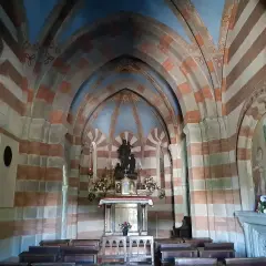 Interno di una cappella con volte a crociera a strisce rosse e bianche. Al centro, un altare con statue e fiori. Un esempio di cosa vedere a Berceto.