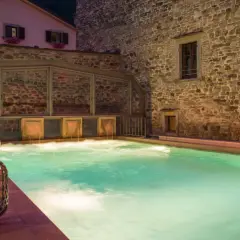 Piscina termale illuminata da lanterne, con cascate d'acqua e un edificio in pietra. Un'oasi di relax che ricorda le terme della Riviera Romagnola.
