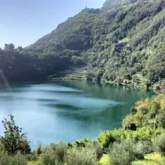 Lago alpino dalle acque verdi, circondato da boschi rigogliosi e terrazzamenti coltivati. Un angolo terme naturale e sereno.