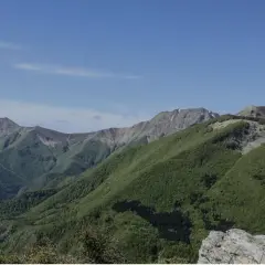 Panoramica dei colli bolognesi in moto, con montagne verdi sotto un cielo azzurro.
