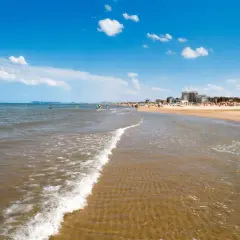 Onda leggera sulla sabbia dorata, con bagnanti e hotel sullo sfondo. Un classico giorno di **mare Emilia Romagna**.