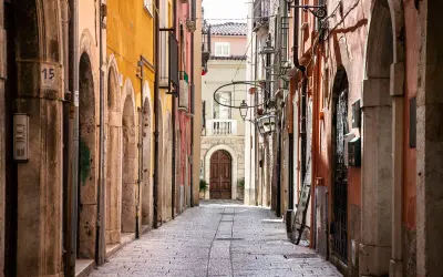 Un vicolo stretto nel chia centro storico, con edifici colorati, archi in pietra e un'antica porta in legno in fondo.