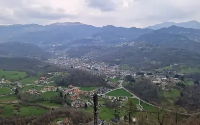 Panoramica della valle Imagna con case sparse tra colline verdi e montagne nebbiose sullo sfondo.