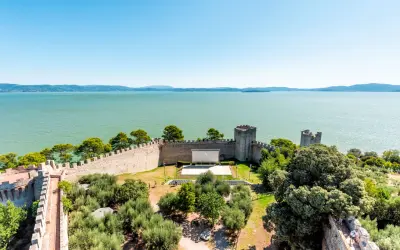Vista dall'alto di un castello con un cinema all'aperto, circondato da ulivi e affacciato sul lago Trasimeno, uno dei borghi vicino Castiglione del Lago.