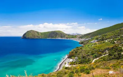 Splendido mare di Lipari con acque cristalline che lambiscono una costa verdeggiante e un borgo bianco.