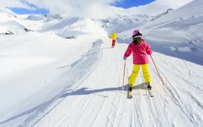 Bambini imparano a sciare su piste da sci per principianti, con montagne innevate sullo sfondo.