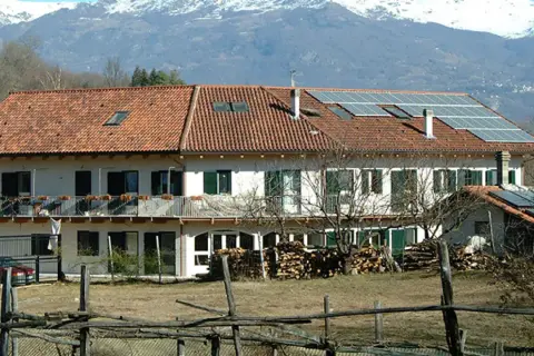 Edificio con pannelli solari, forse parte della comunità Damanhur, con montagne innevate sullo sfondo.
