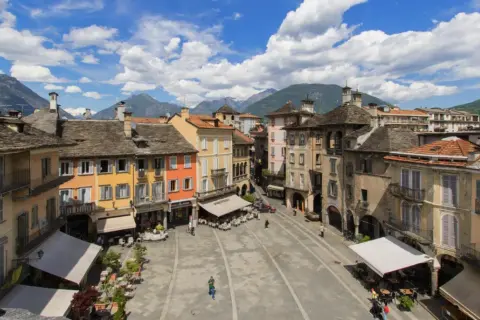Piazza colorata con montagne sullo sfondo, un assaggio di dove si trova Domodossola.