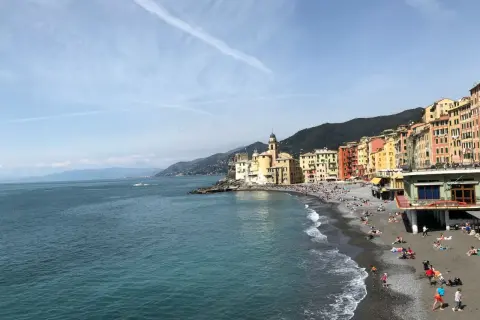 Un angolo di **mare vicino Milano**, con case colorate affacciate su una spiaggia di ciottoli e gente che prende il sole.