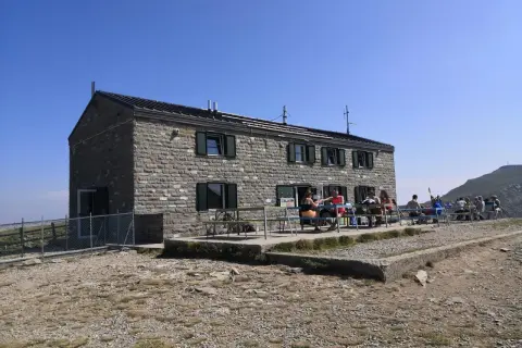 Rifugio in pietra con persone sedute ai tavoli all'esterno, un luogo ideale per una pausa durante un'escursione nei rifugi Emilia Romagna.