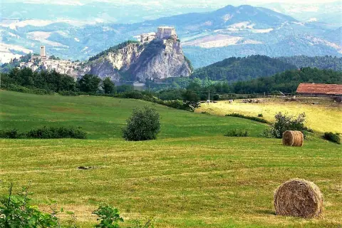 Colline romagnole dove andare: un borgo arroccato su uno sperone roccioso, campi verdi e balle di fieno.