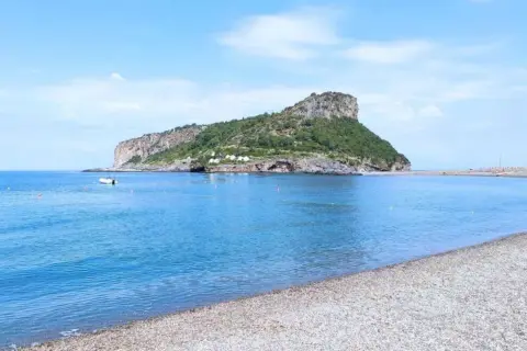 Acque azzurre e una spiaggia di ciottoli nel **golfo di Policastro**, con un'isola verdeggiante sullo sfondo.