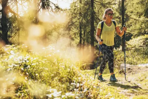 Giovane donna con bastoncini da trekking si gode le sue passeggiate Trentino in un bosco soleggiato.