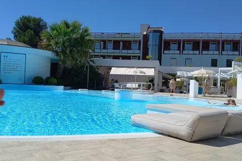 Piscina azzurra e lettini prendisole in un resort, con un edificio moderno sullo sfondo. Un'oasi di benessere e relax, perfetta per godersi le terme Viterbo Salus.