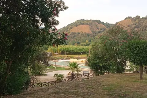 Un angolo di pace ad Agnano, dove si trova un complesso con piscine e vegetazione lussureggiante, incorniciato da colline verdi.