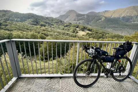 Bicicletta da cicloturismo pronta per esplorare l'Appennino Tosco Emiliano, con un panorama mozzafiato di boschi e montagne.