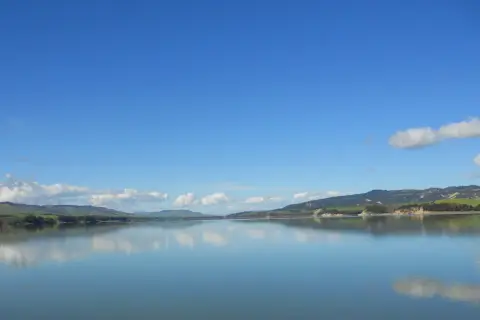 Lago calmo con riflessi di colline verdi e cielo azzurro. Un'ottima meta per scoprire cosa vedere vicino Matera.