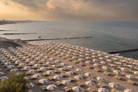 Filetto di sabbia dorata con file ordinate di ombrelloni e lettini, bagnato dal mare del Friuli Venezia Giulia al tramonto.