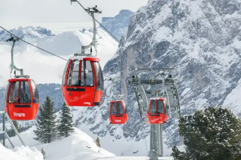 Cabine rosse su un impianto di risalita in Trentino, perfette per esplorare le località sciistiche economiche. Montagne innevate e pini sullo sfondo.