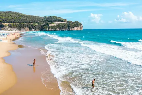 Spiaggia dorata con onde azzurre, scogliere verdi e un castello in cima. Perfetto per chi cerca il mare nel Lazio dove andare.