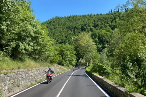 Motociclisti sfrecciano su strade panoramiche dell'Emilia Romagna, tra colline verdi e cielo azzurro.