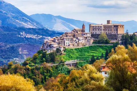 Borgo medievale su una collina verde, con montagne sullo sfondo. Un gioiello di montagna vicino Roma, con case antiche e un castello imponente.