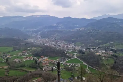 Panoramica della valle Imagna con case sparse tra colline verdi e montagne nebbiose sullo sfondo.