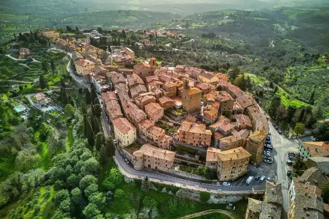 Vista aerea del borgo Panicale in Umbria, con le sue case in pietra e tetti rossi che si aggrappano alla collina, circondato da verdi colline.