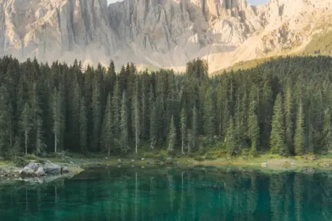 Lago alpino con riflessi di bosco di conifere e montagne imponenti. Un luogo ideale per lo sport e natura.