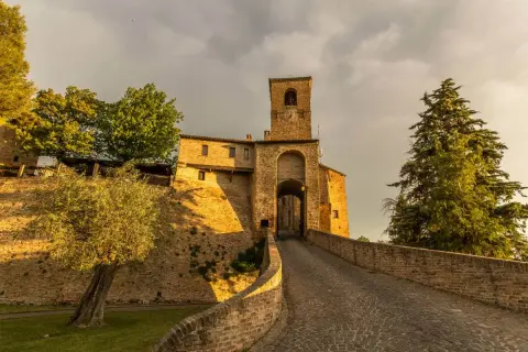 Antica porta di Montegridolfo cosa vedere: un borgo medievale con torre campanaria e vicoli acciottolati, immerso nel verde.